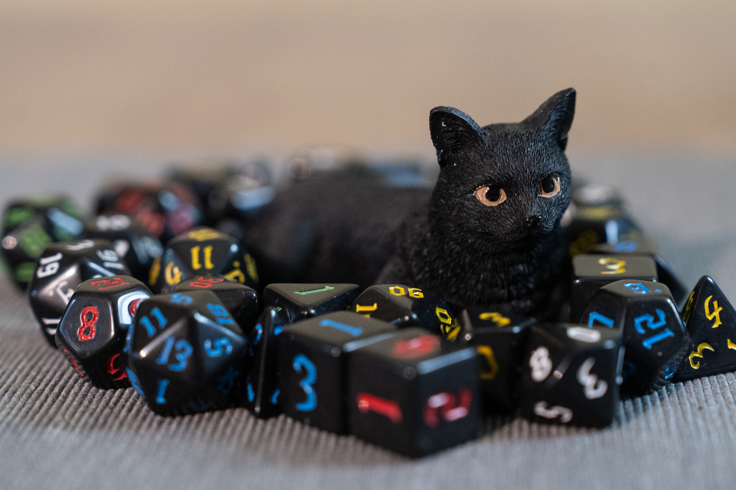 Black cat figurine lying among dungeons and dragons (aka dnd or d&d) game dice sets, including 1d20, d12, d10, d8, d6, d4