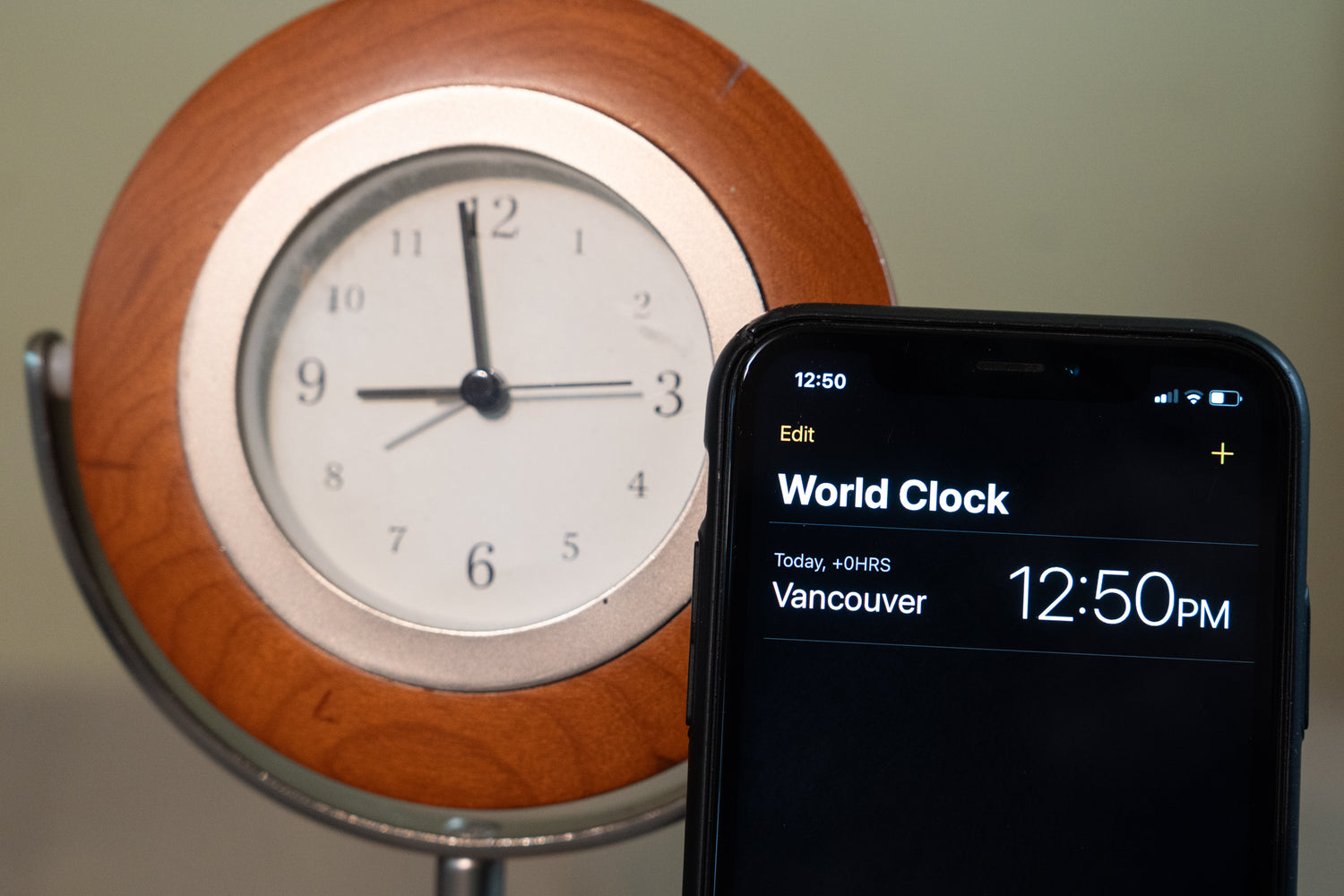broken wooden clock and smartphone displaying world clock app with correct time.