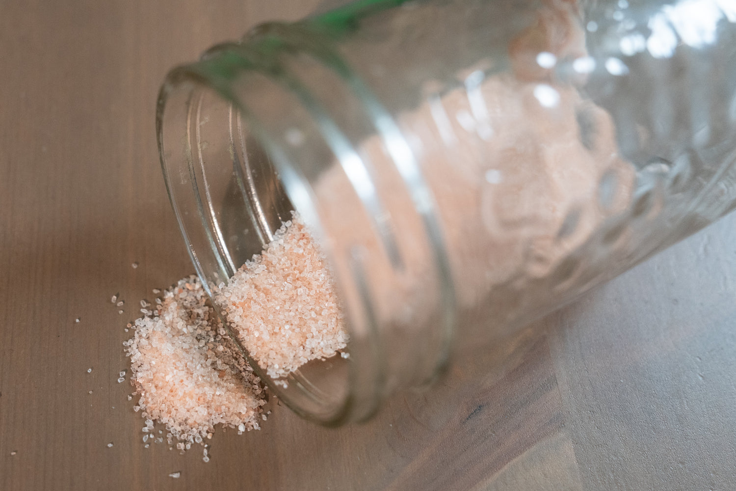 Glass jar with pink Himalayan salt spilling out onto a wooden table