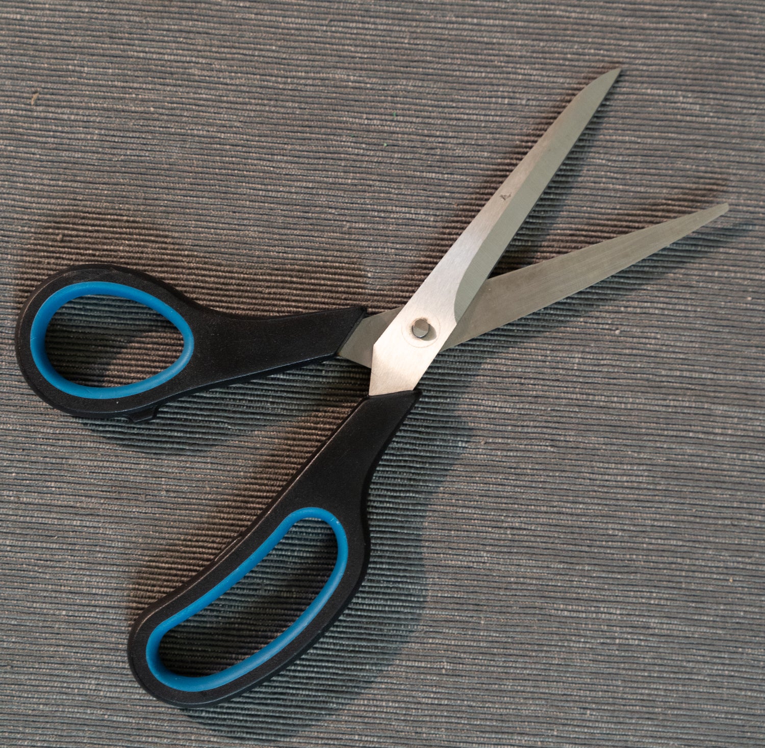 opened scissors with black handles and blue accents on a textured gray surface