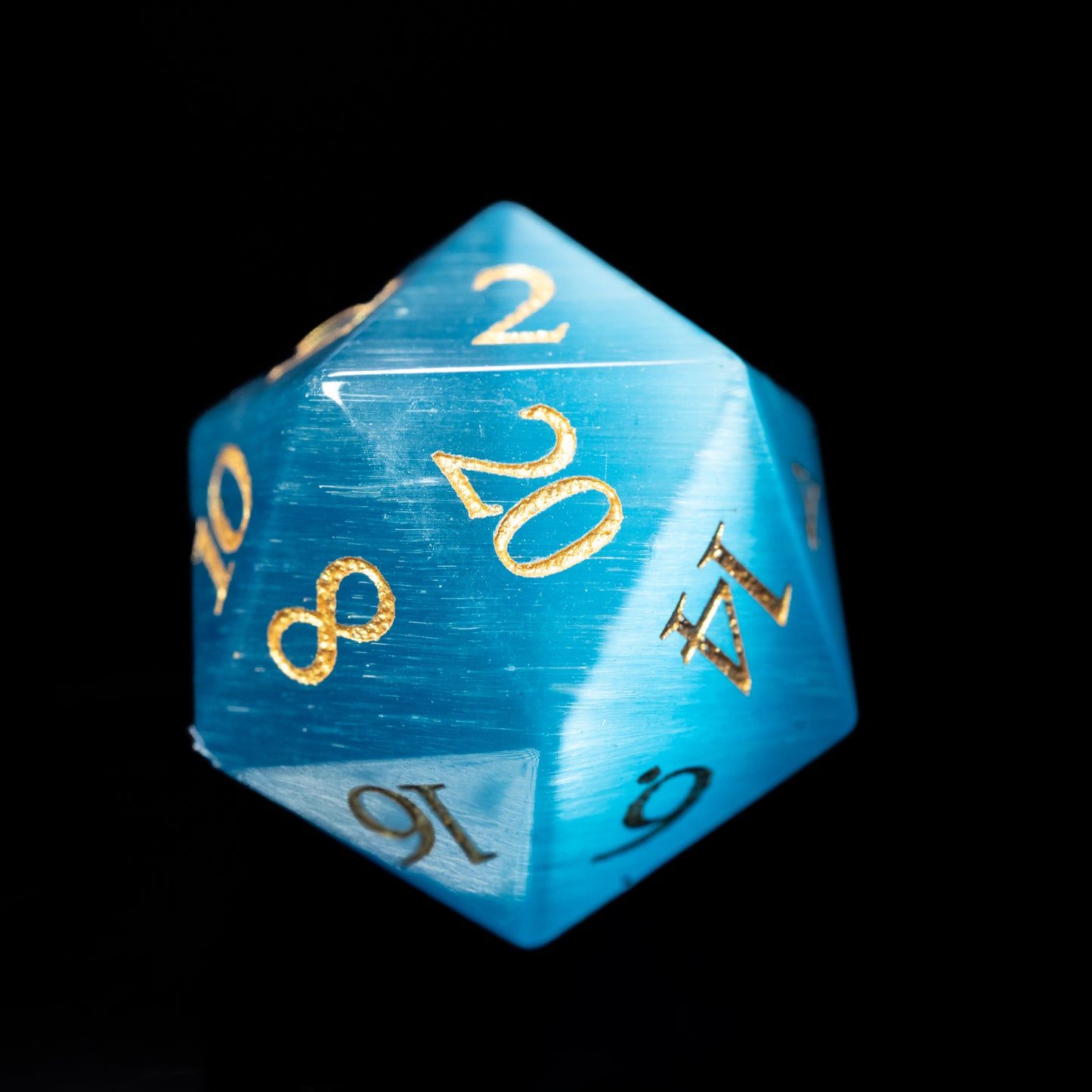 Blue cat's eye glass gemstone dungeons and dragons (aka dnd or d&d) d20 game die or dice with gold numbers on a black background