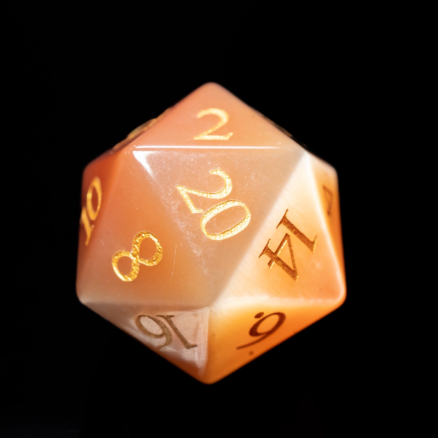 orange cat's eye glass gemstone dungeons and dragons (aka dnd or d&d) d20 game die or dice with gold numbers on a black background
