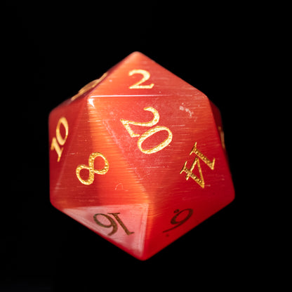 Red cat's eye glass gemstone dungeons and dragons (aka dnd or d&d) d20 game die or dice with gold numbers on a black background