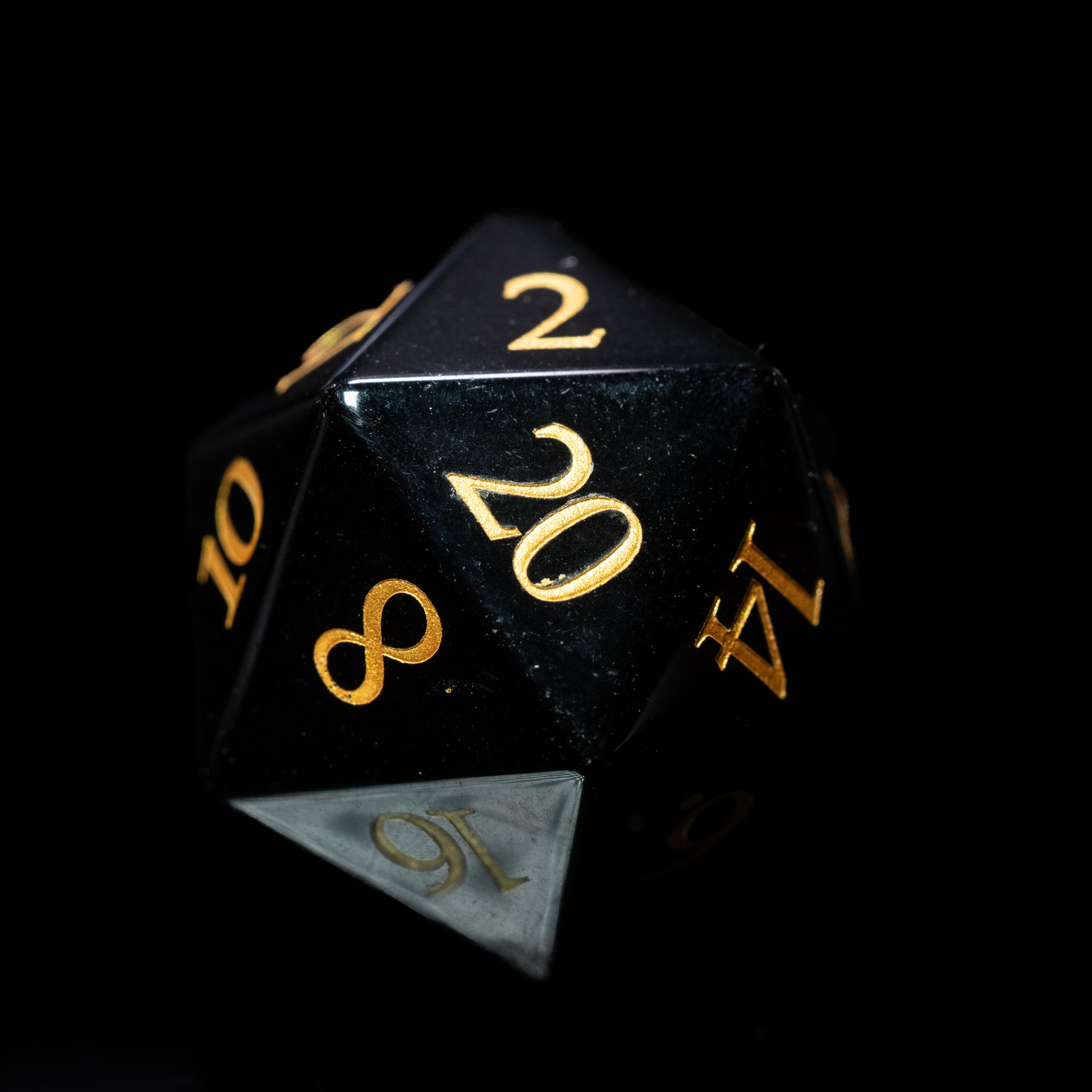 Black obsidian glass gemstone dungeons and dragons (aka dnd or d&d) d20 game die or dice with gold numbers on a black background