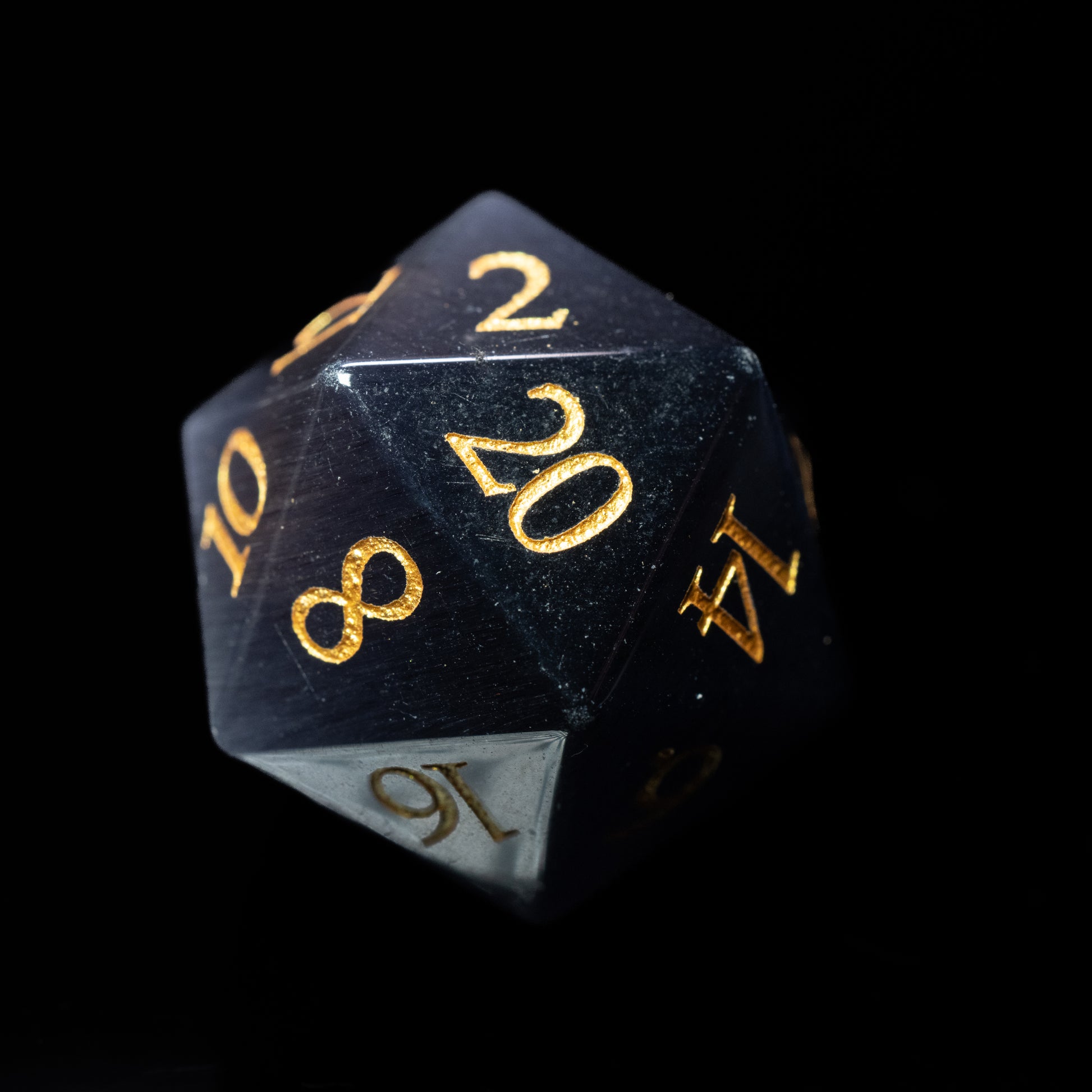 deep purple cat's eye gemstone dungeons and dragons (aka dnd or d&d) d20 game dice or die with gold numbers on a black background